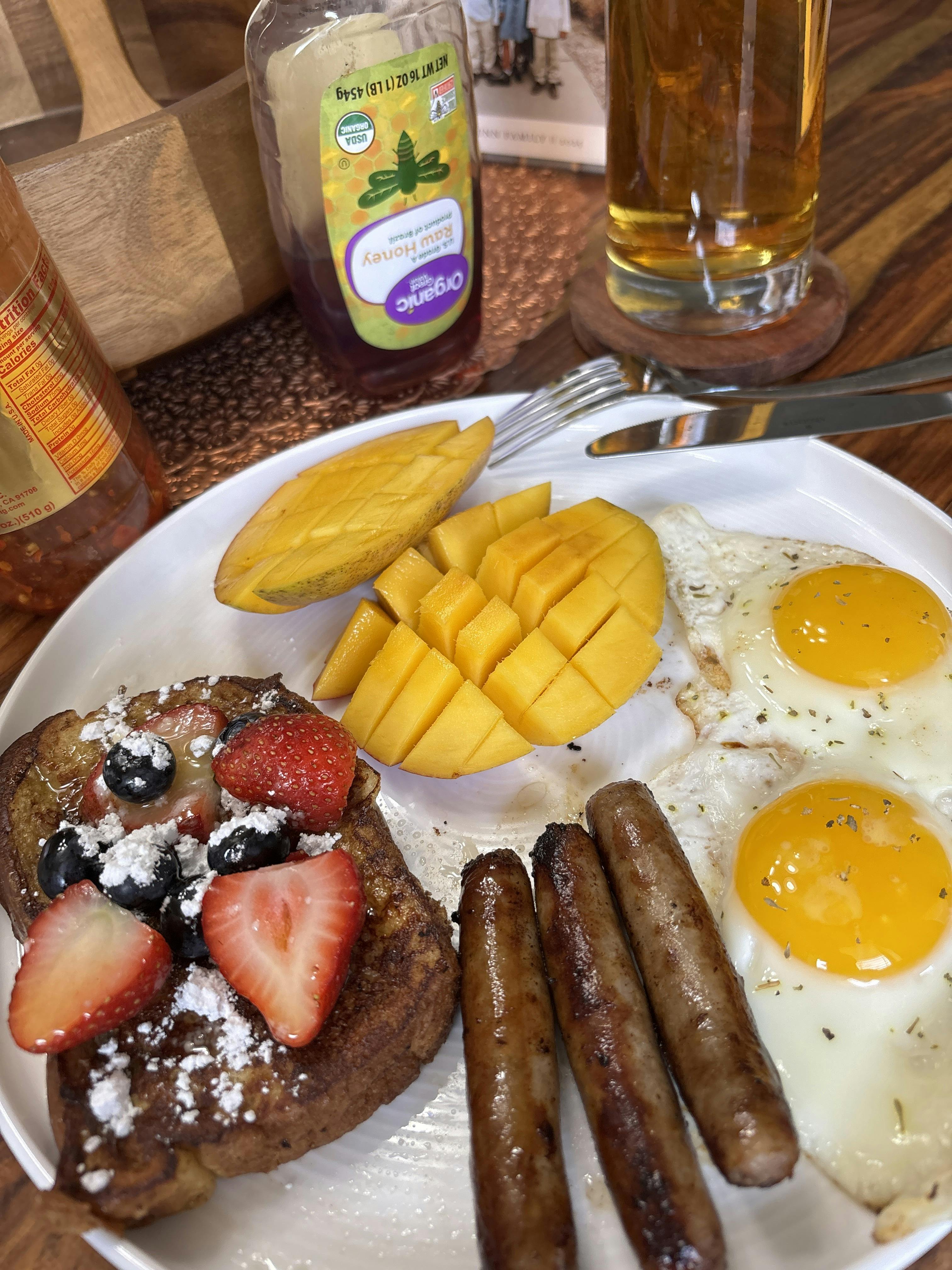 French toast with berries, eggs, sausage, and mango slices on a plate