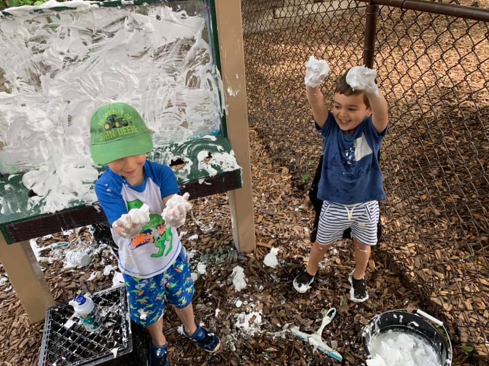 Two children playing with shaving cream outdoors
