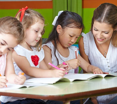 Adult and three children writing in books at a table