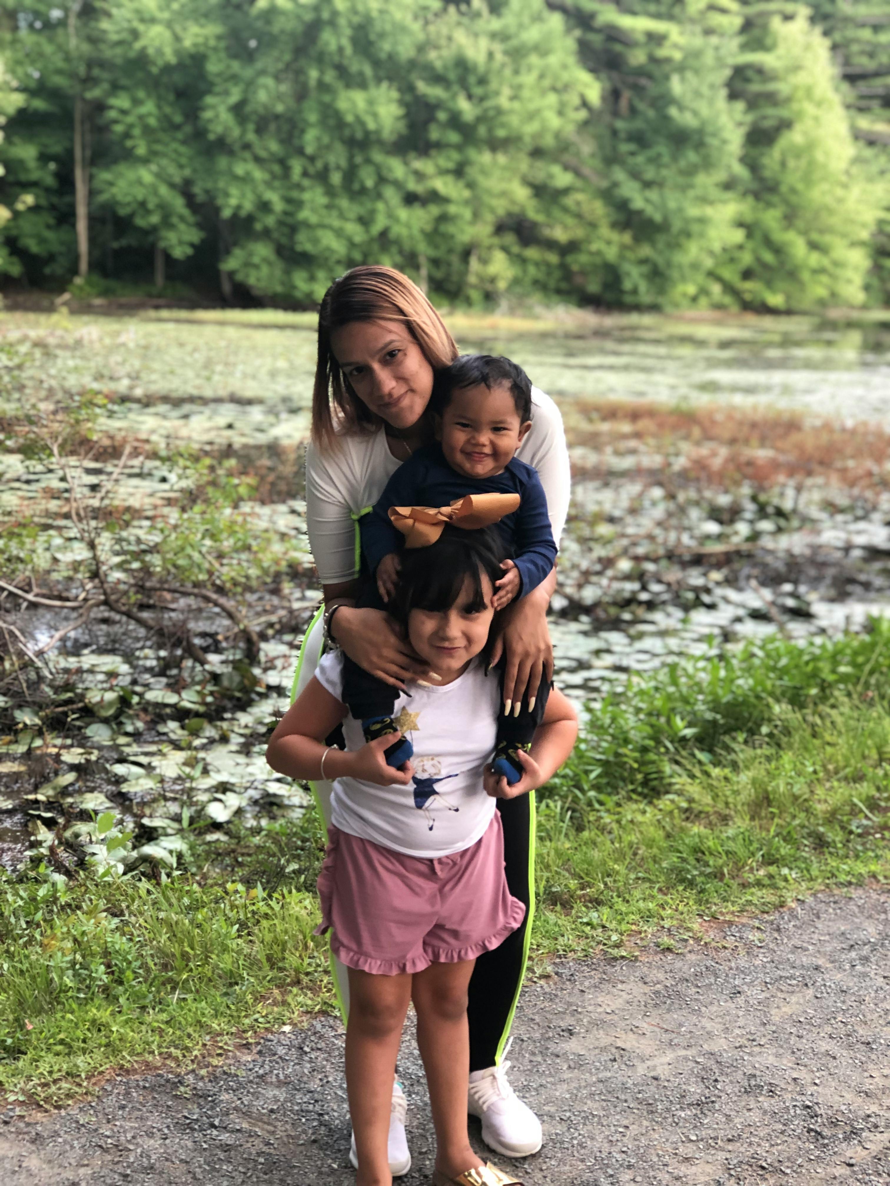 Person holding two children, one on shoulders, near a pond