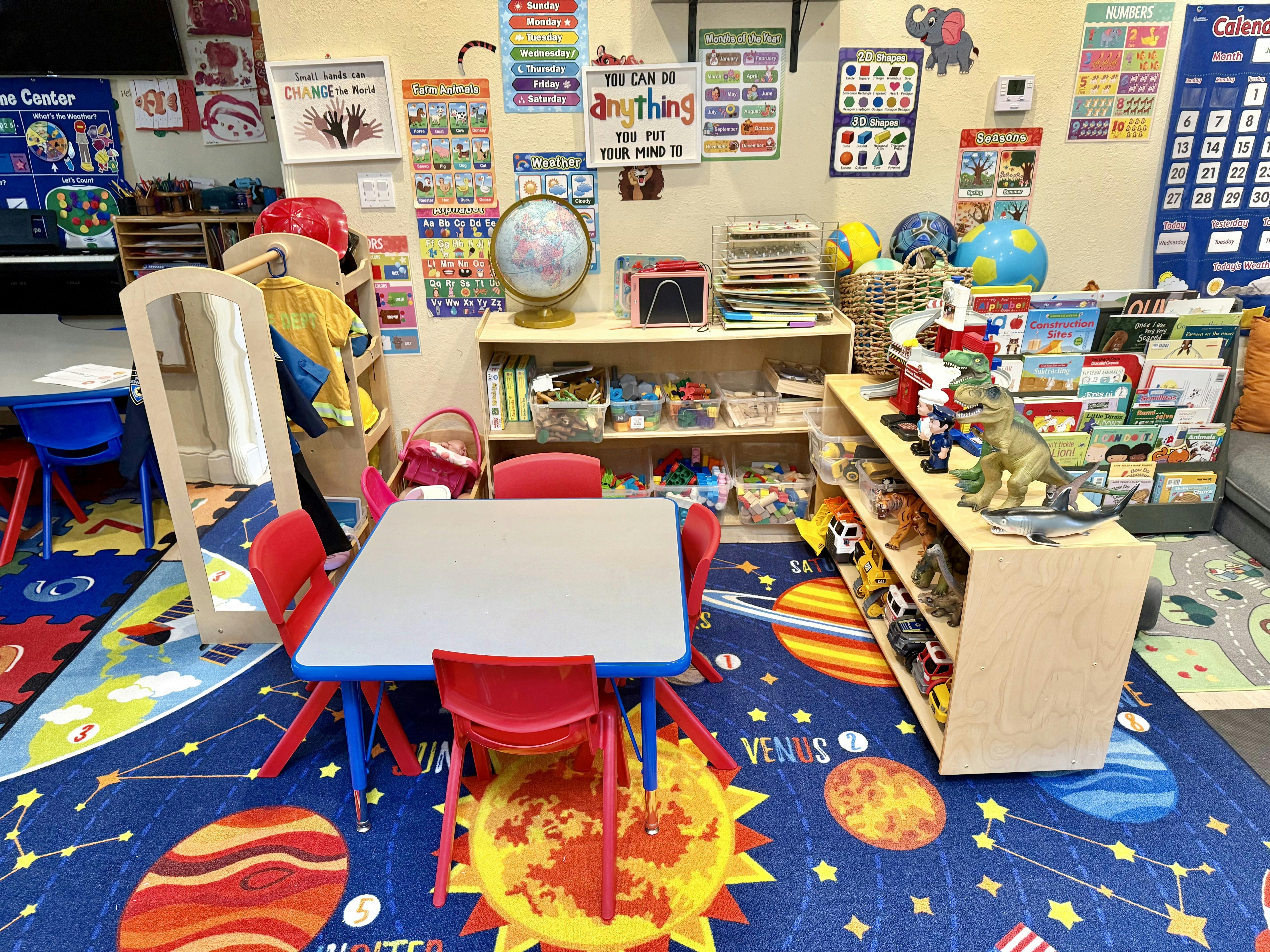 Classroom with small tables and chairs, shelves with toys and books