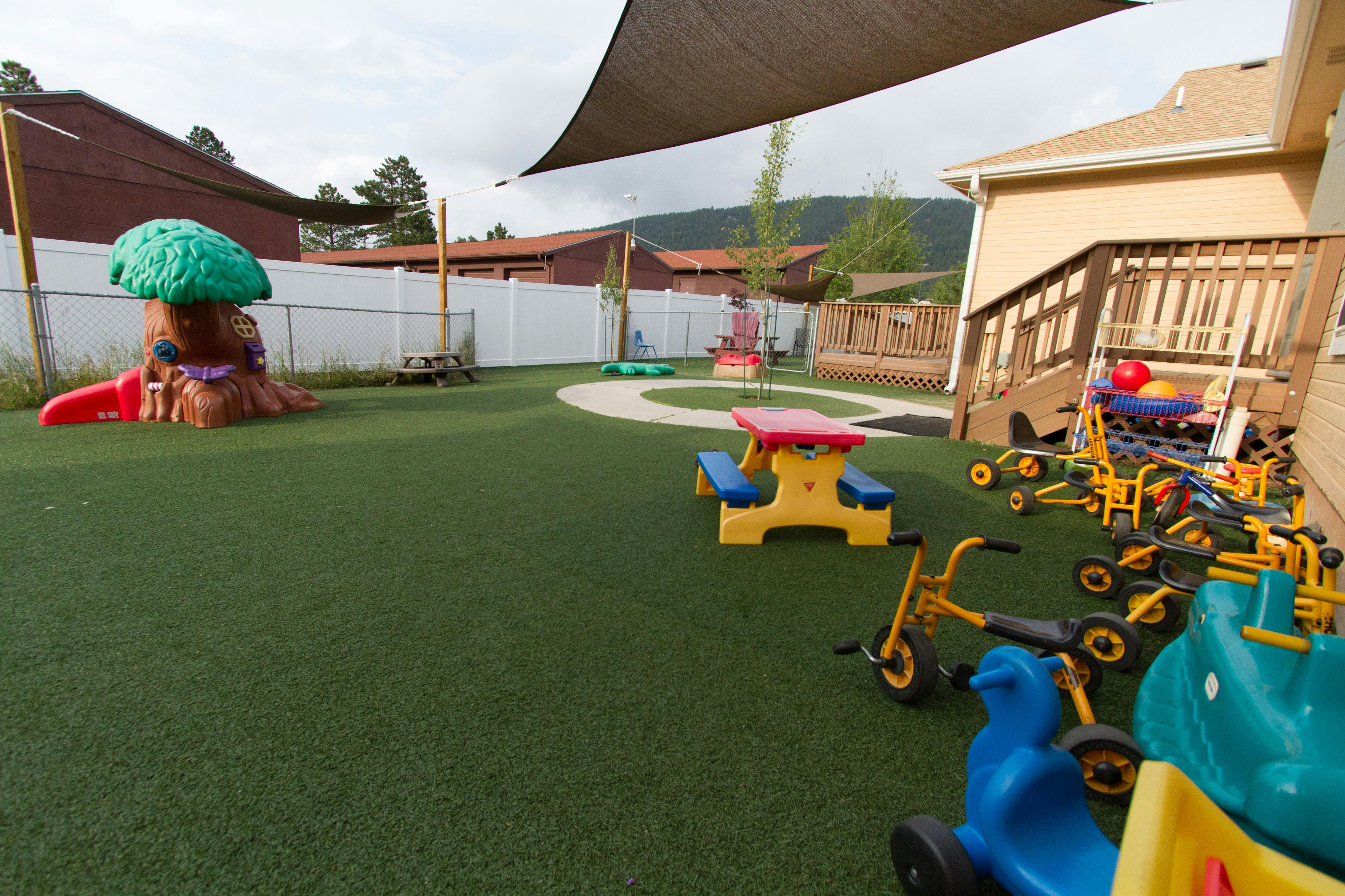 Outdoor playground with artificial turf, play structures, and tricycles