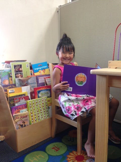 Child sitting in a chair holding a book in a classroom