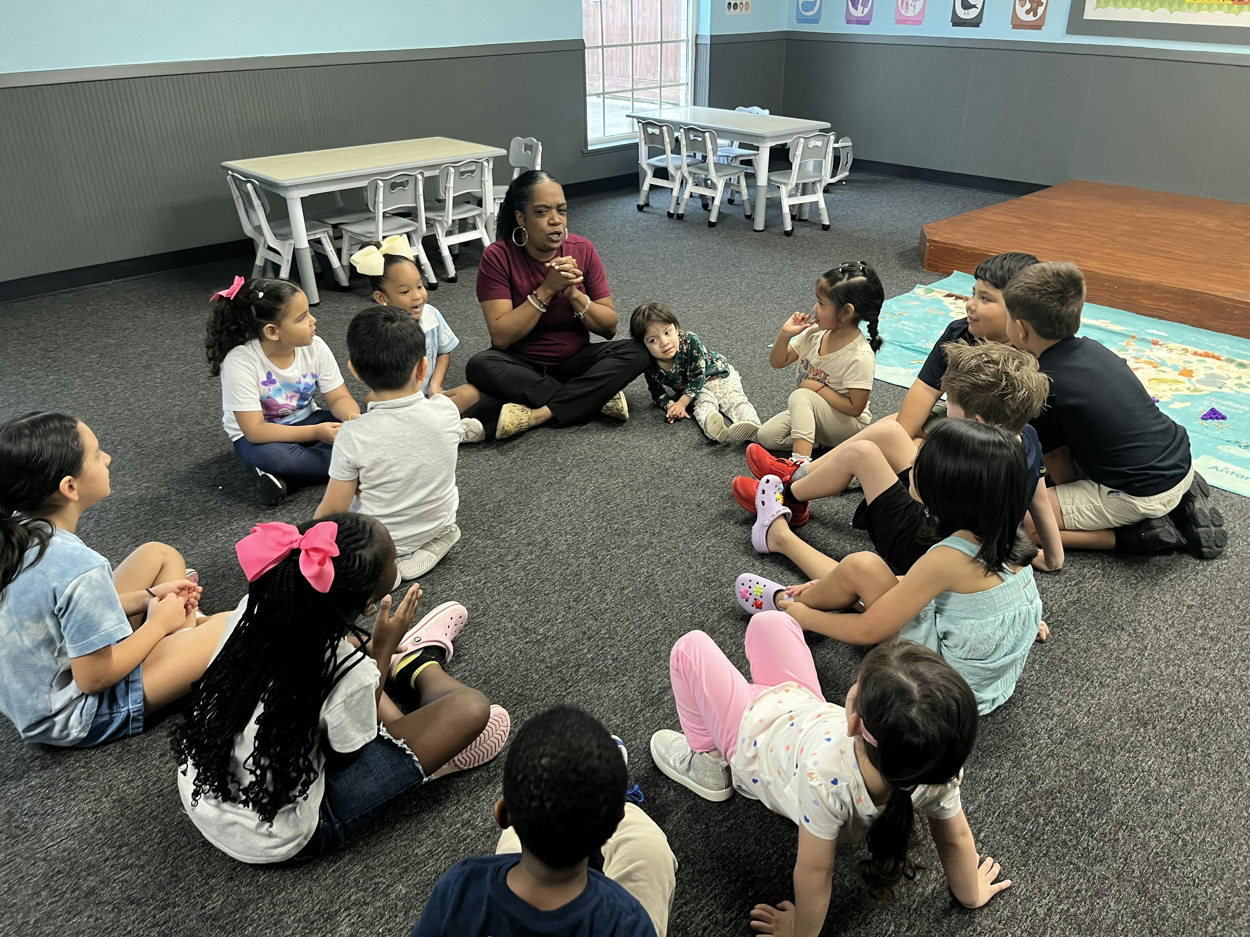 Adult sitting on the floor in a circle with a group of children in a classroom