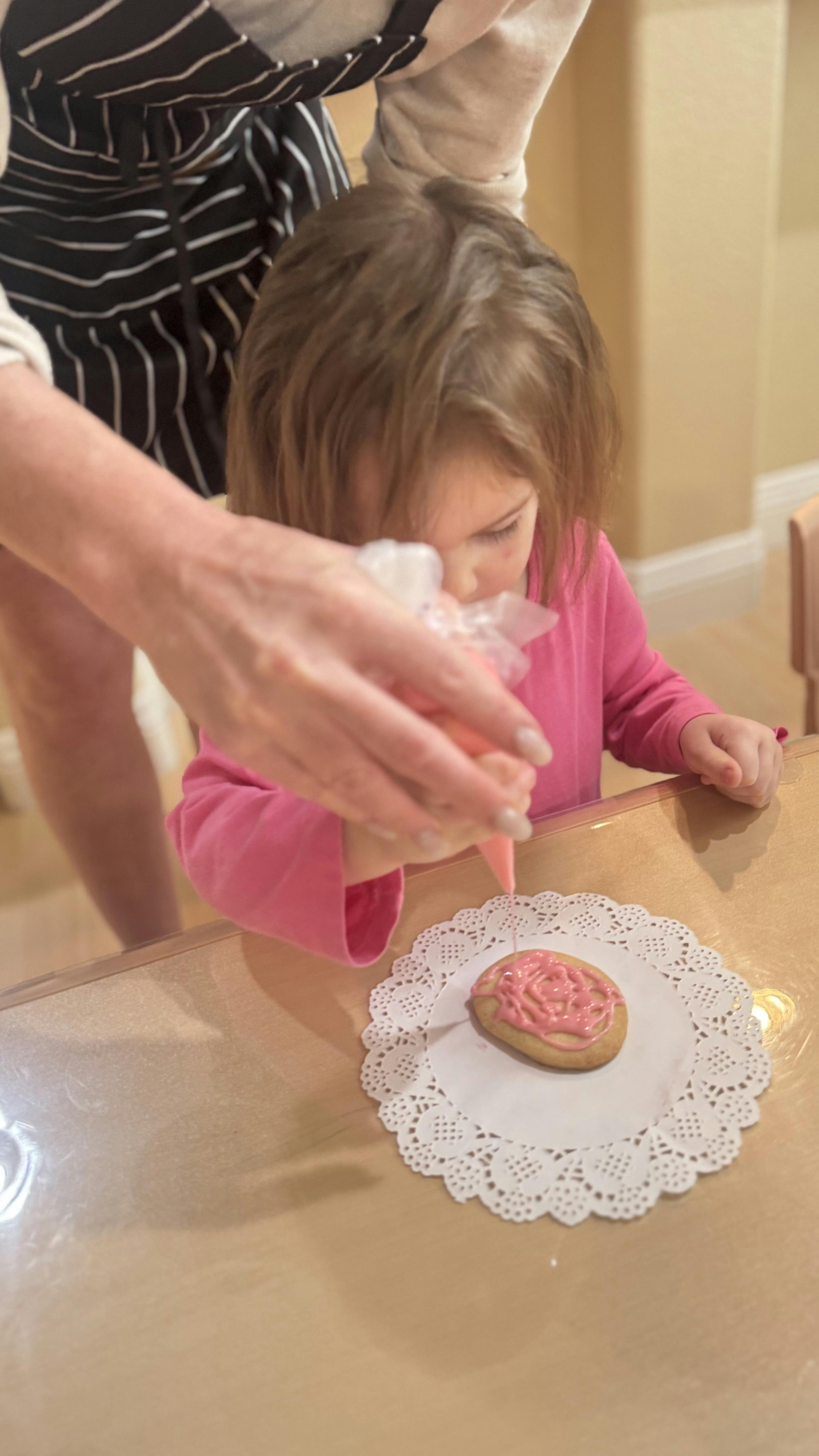 Person's hands icing a cookie with a child watching