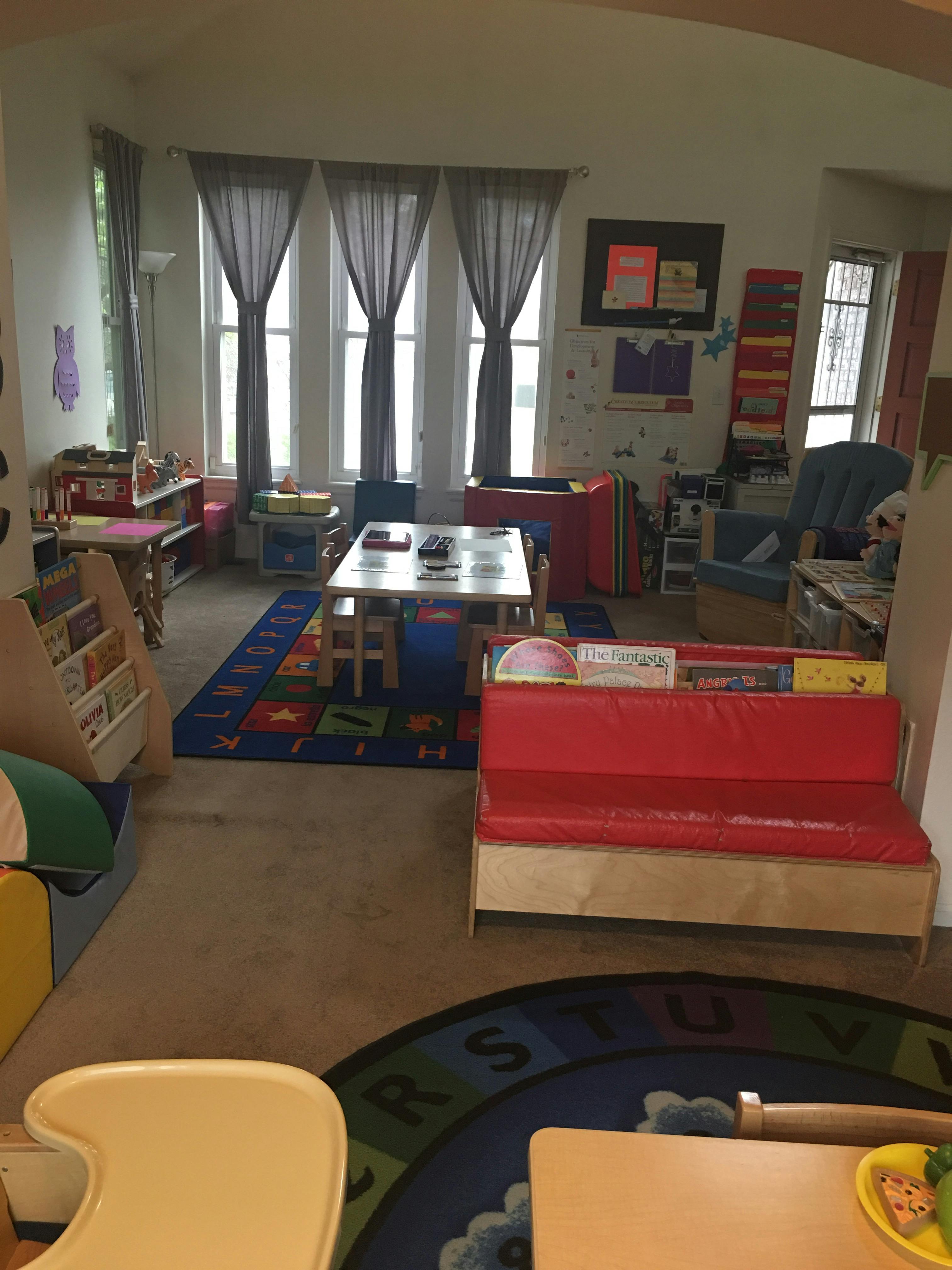 A classroom with small tables and chairs, a colorful rug, and a red bench