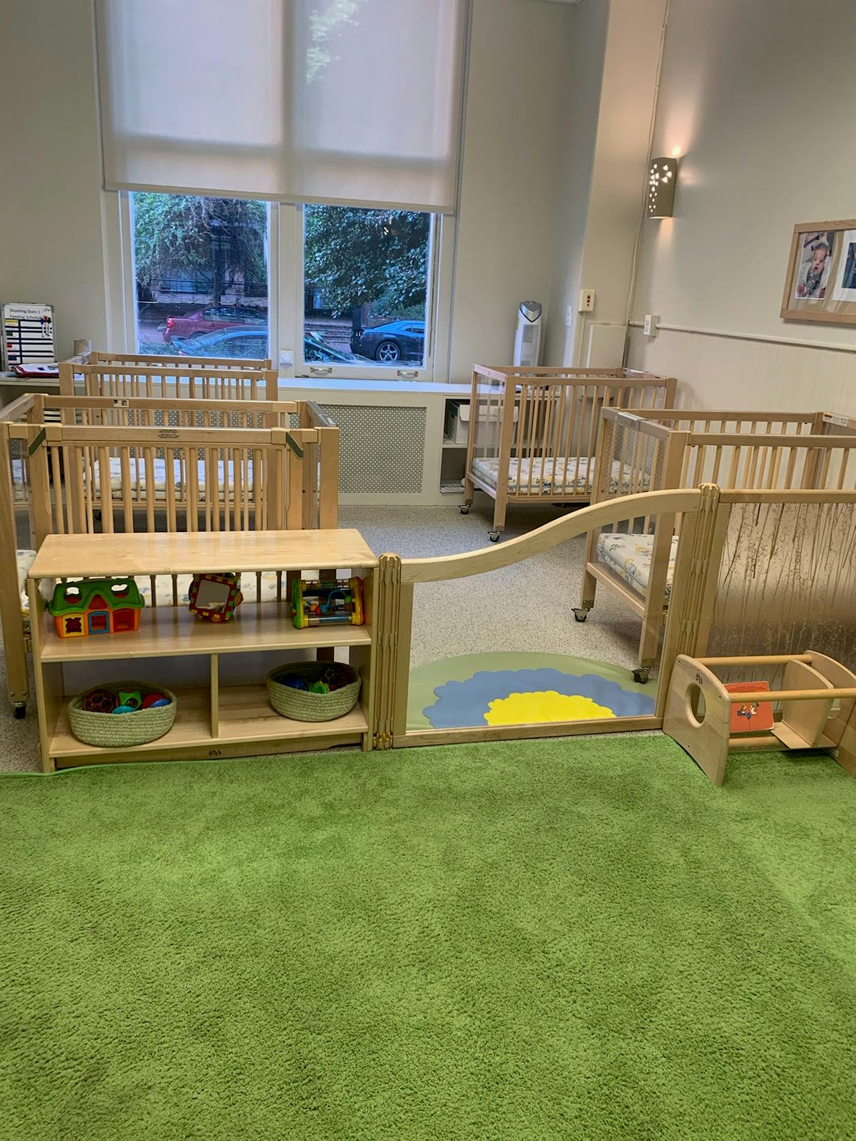 Nursery room with multiple cribs and a play area with a green rug