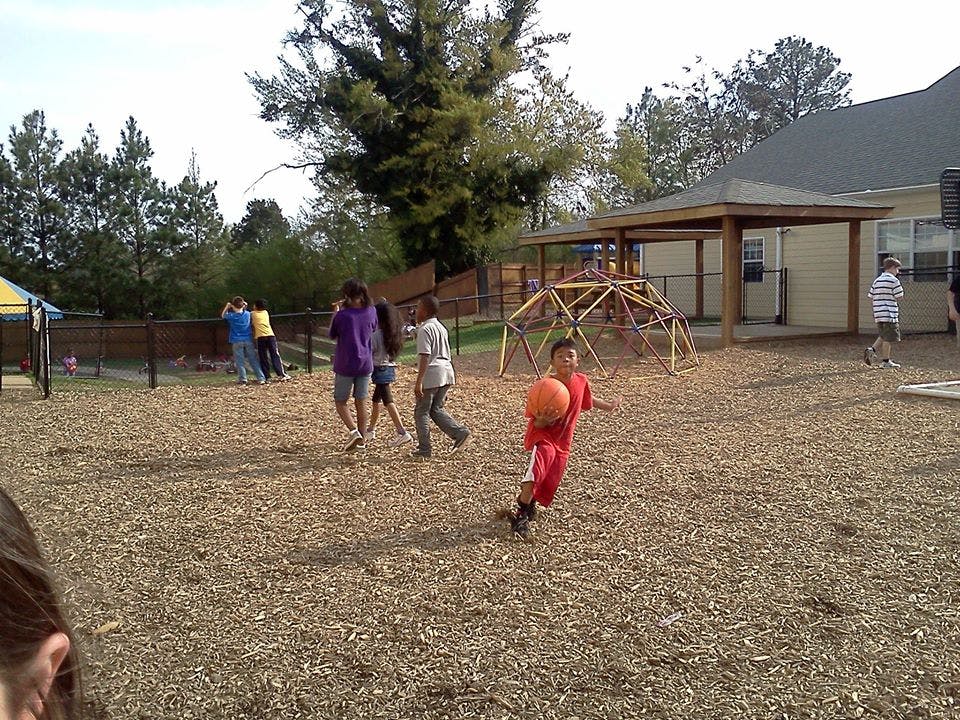 Child in red holding a basketball on a playground with other children