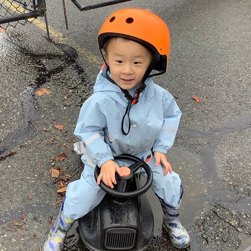 Child in rain suit and helmet on a ride-on toy