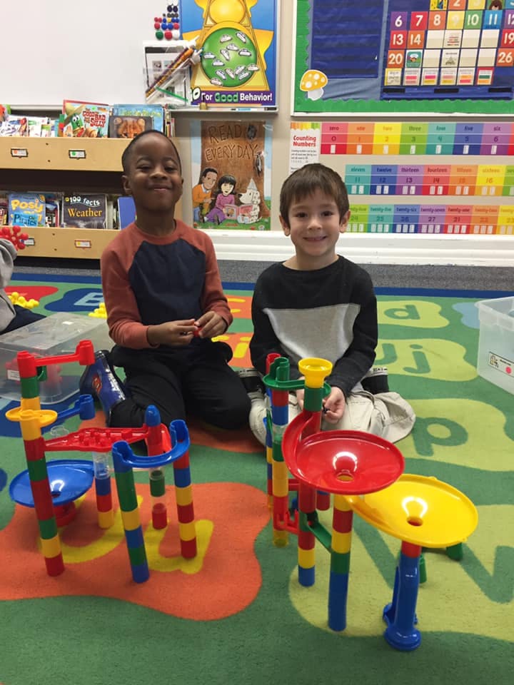 Two children playing with colorful marble run toys in a classroom