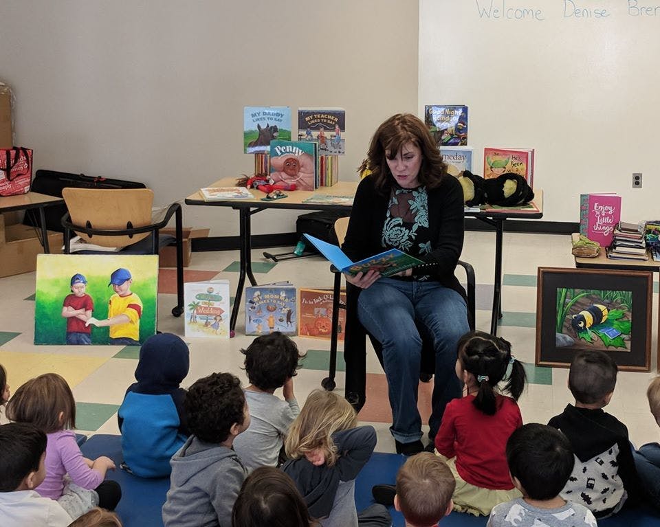 Person reading a book to a group of children sitting on the floor
