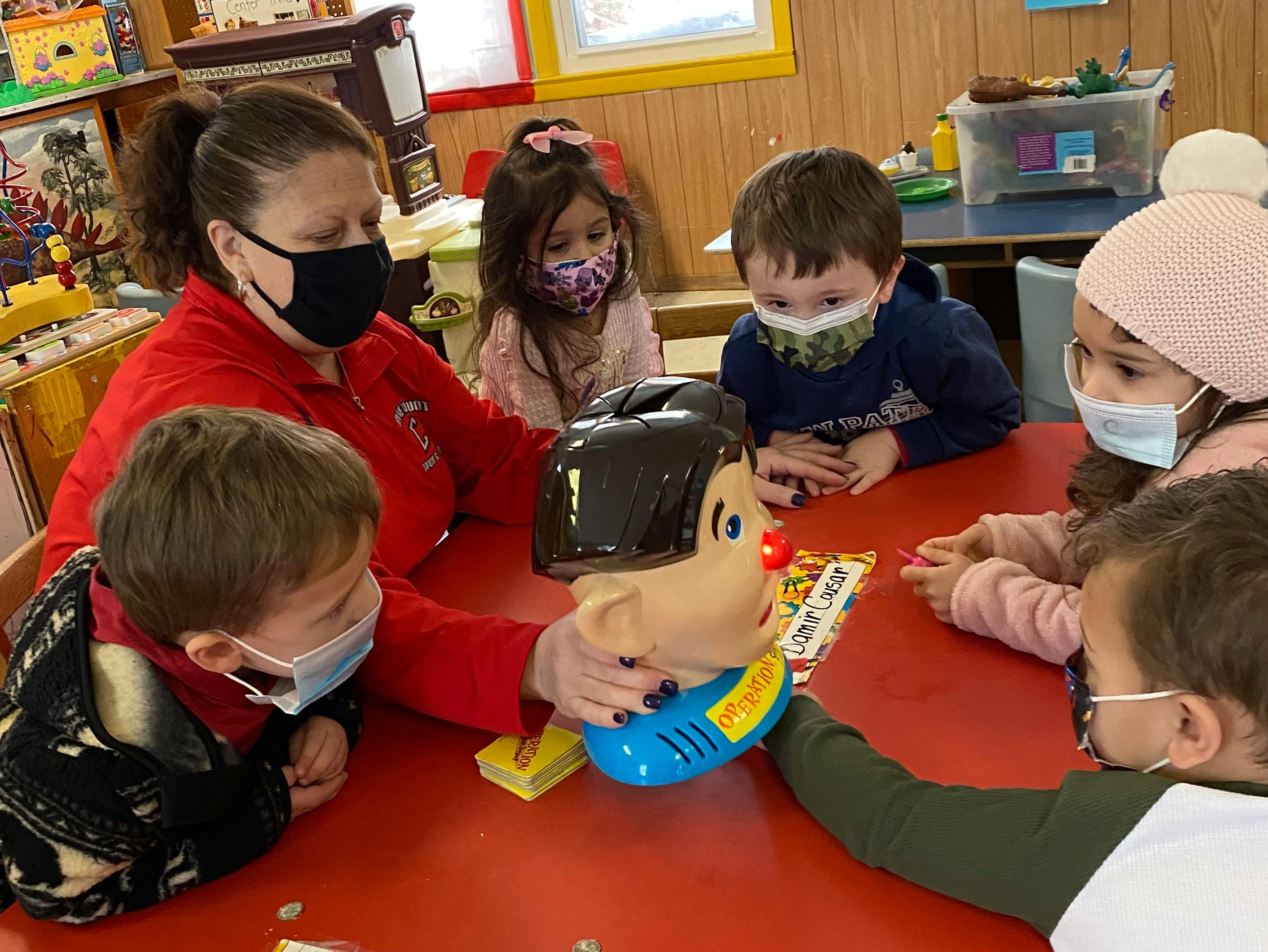 Adult and children in masks playing a game at a table