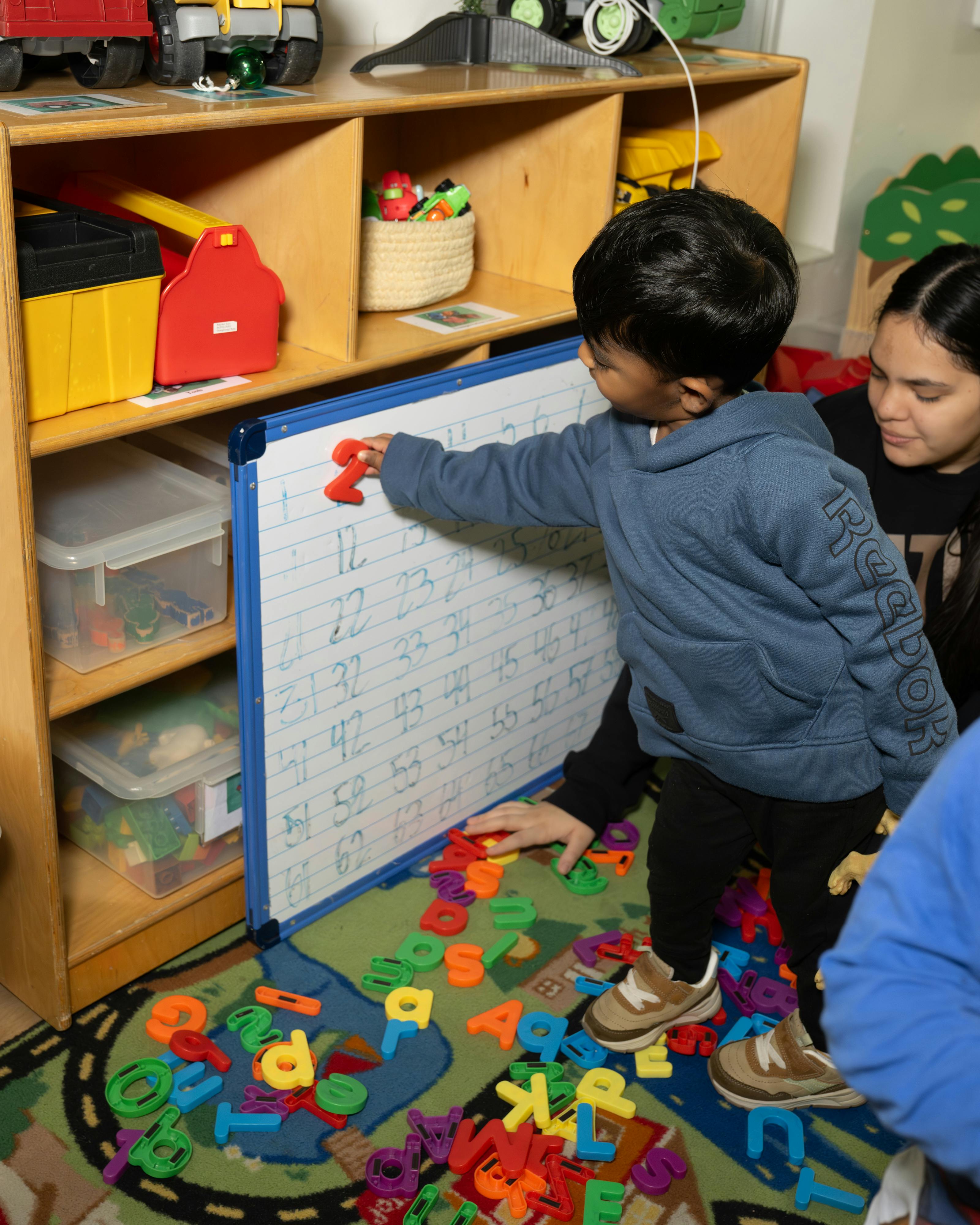 Child placing a magnetic letter on a whiteboard in a classroom