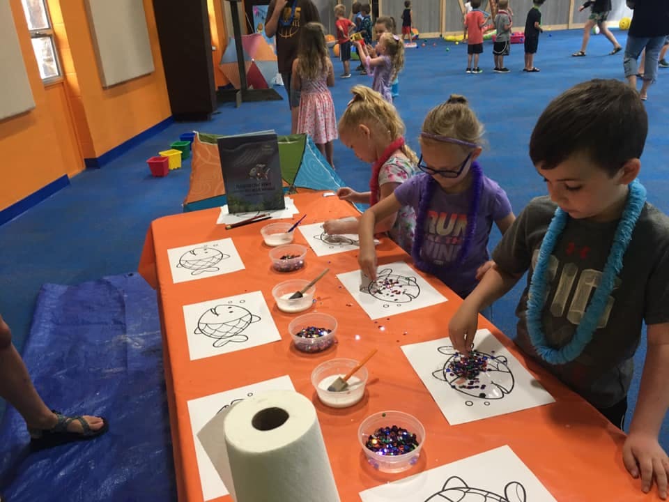 Children decorating turtle drawings with glitter at a table