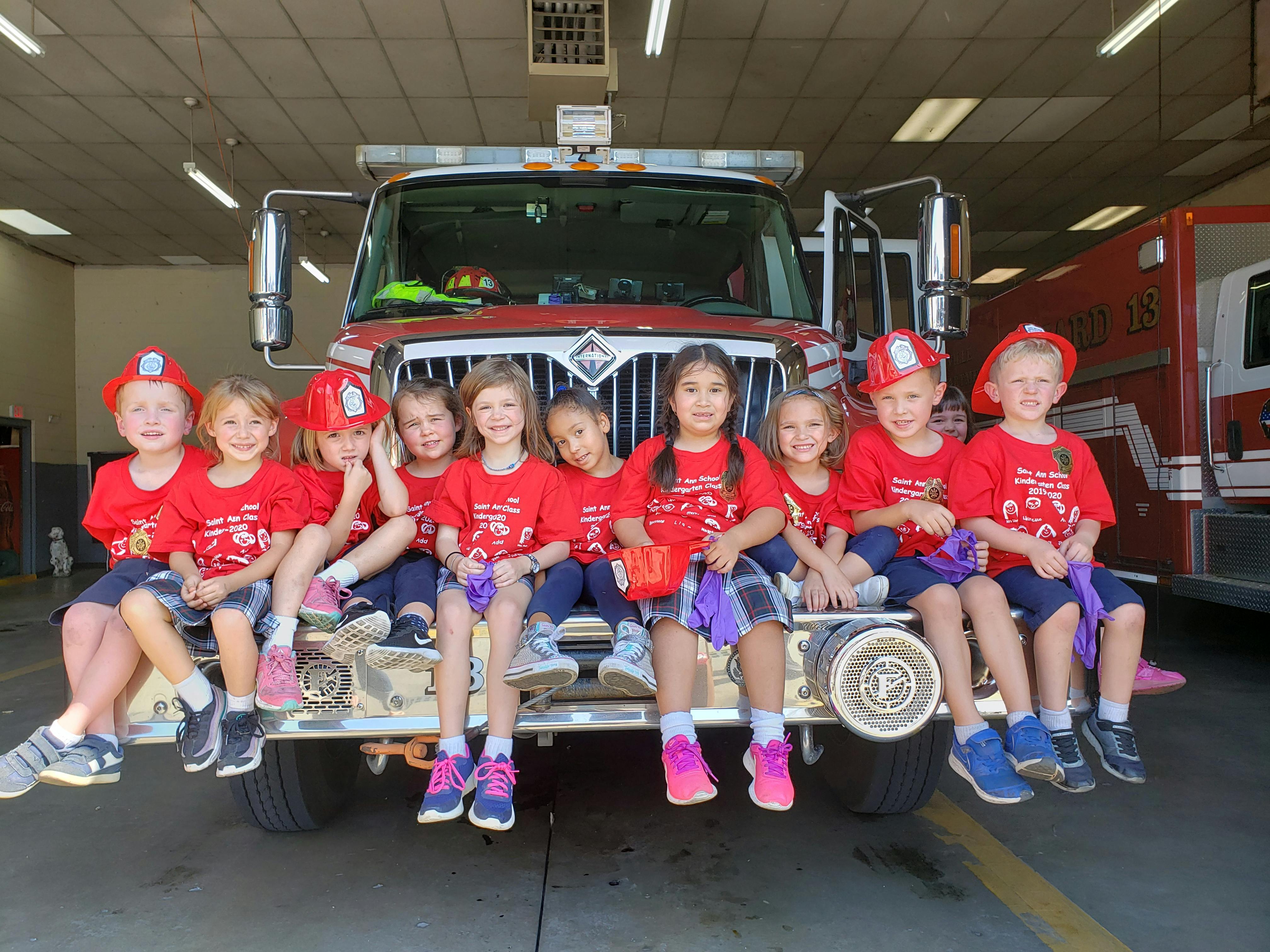 Children in red shirts and fire hats sitting on a fire truck