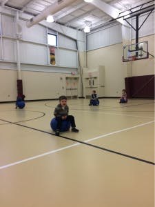 Children sitting on blue exercise balls in a gymnasium