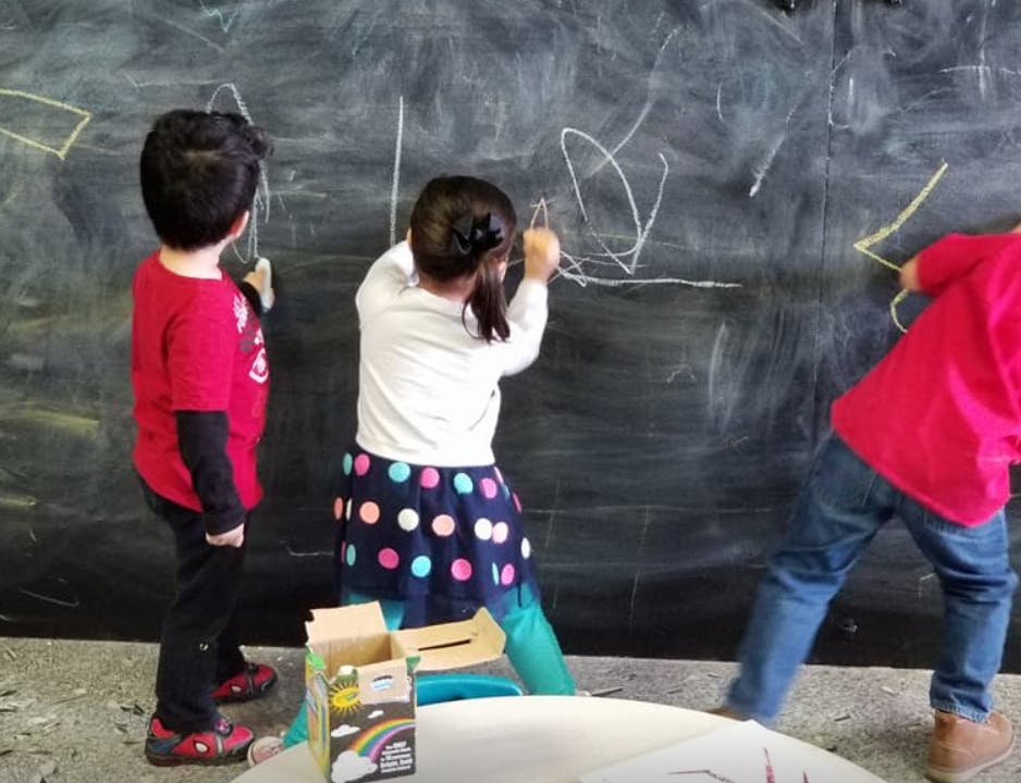 Three children drawing on a large chalkboard