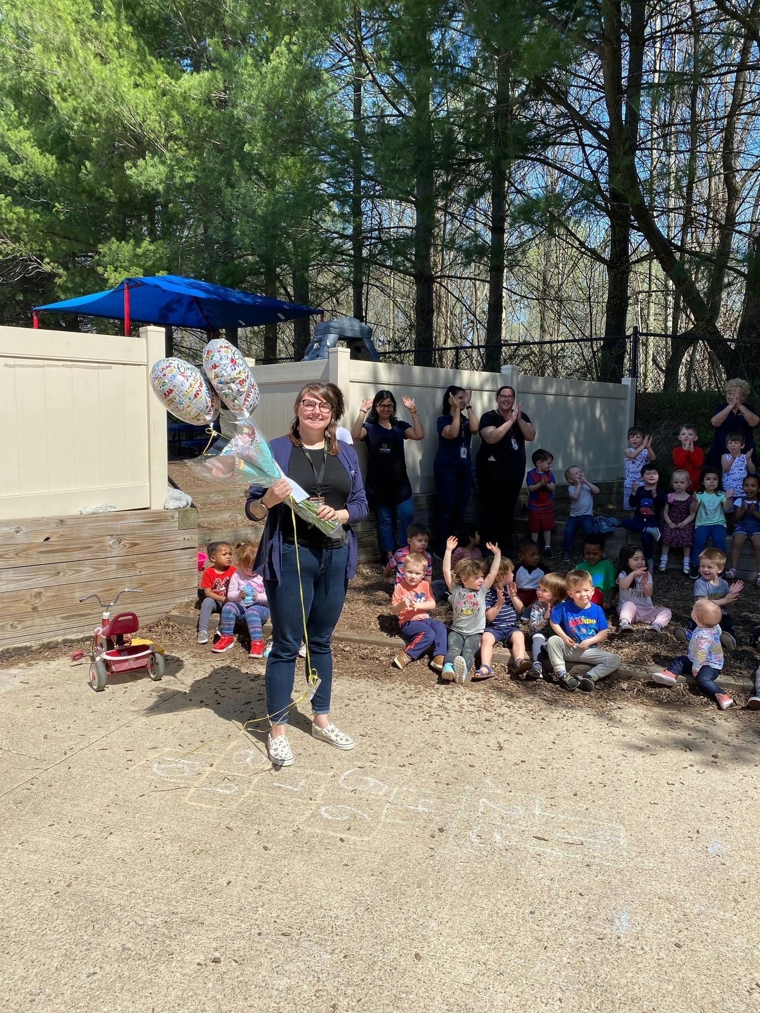 Person holding balloons and flowers with children and adults in background