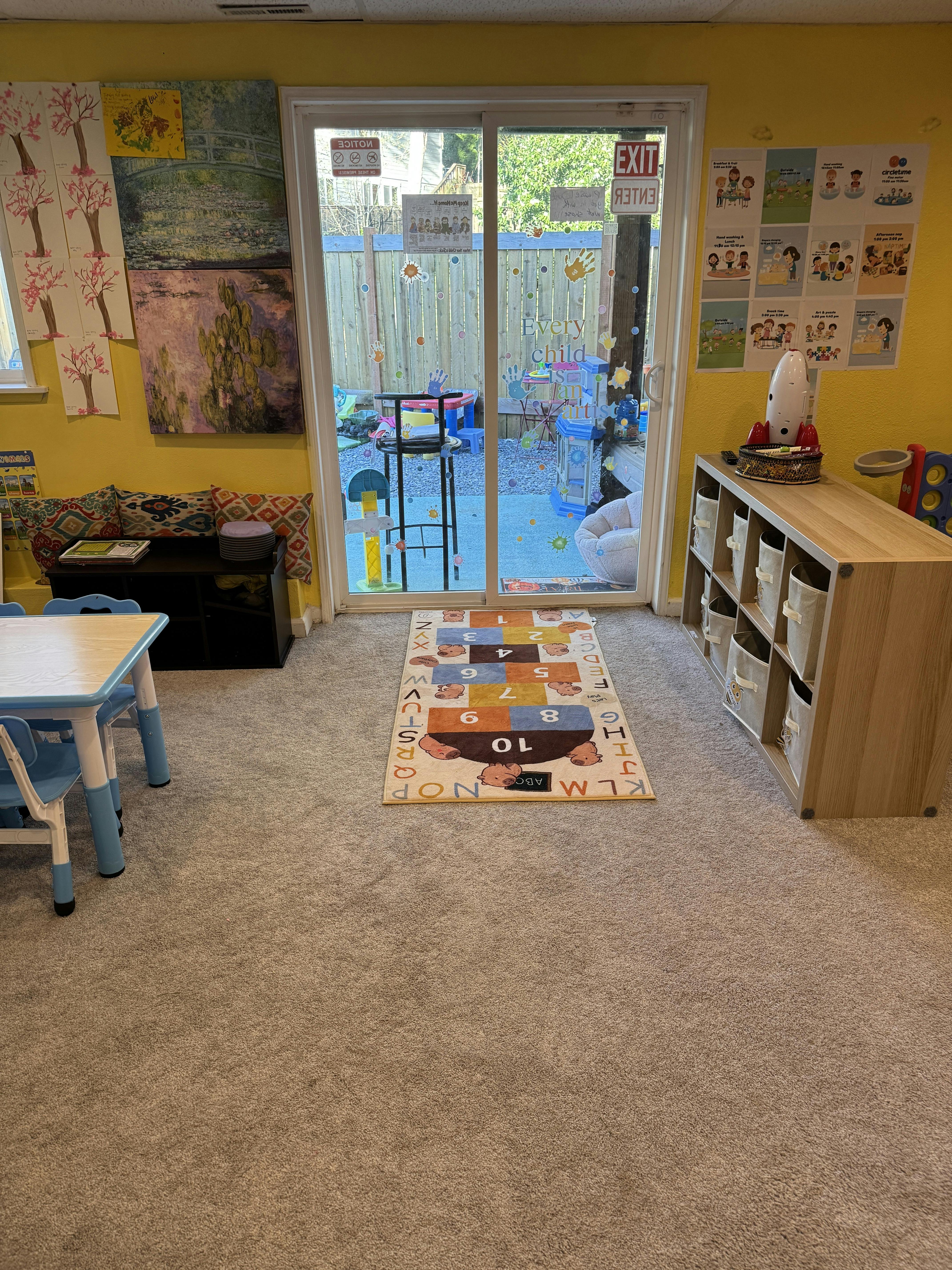 Childcare playroom with a small table, shelves, and a sliding door to a backyard