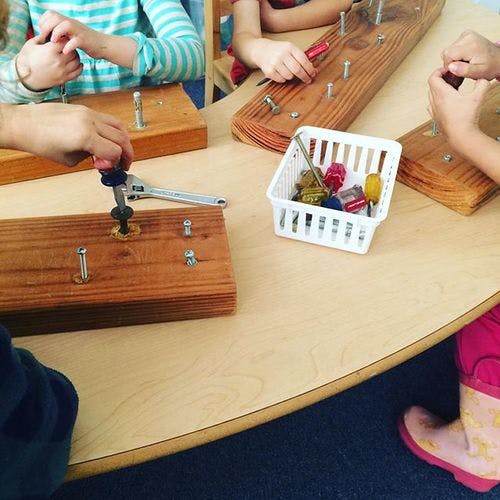 People using wrenches and screwdrivers on wooden boards with bolts and screws