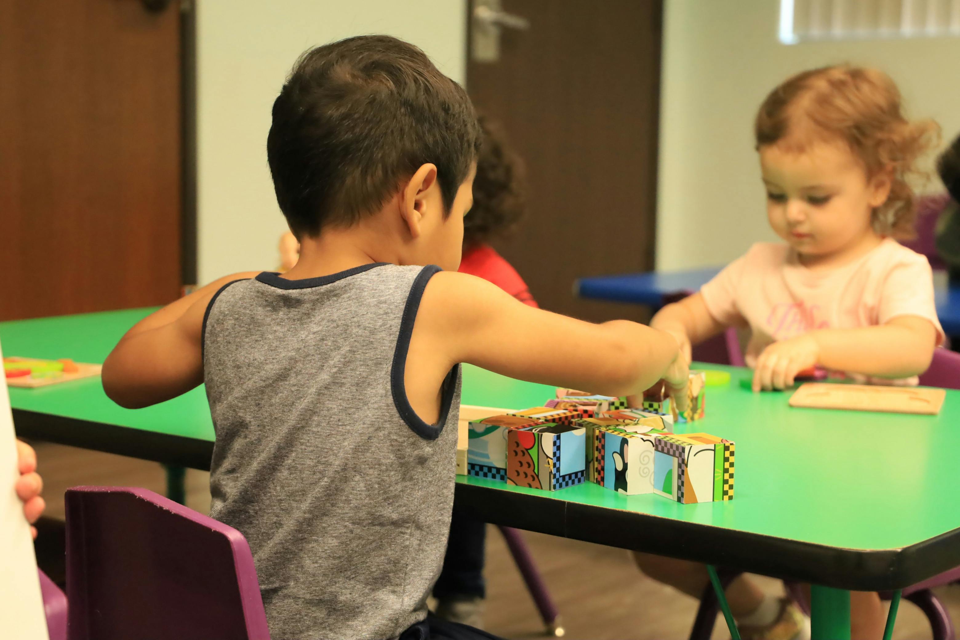Two children playing with blocks at a green table