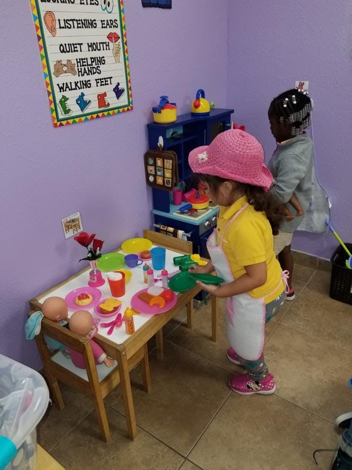 Child in a pink hat and apron playing with toy dishes at a table