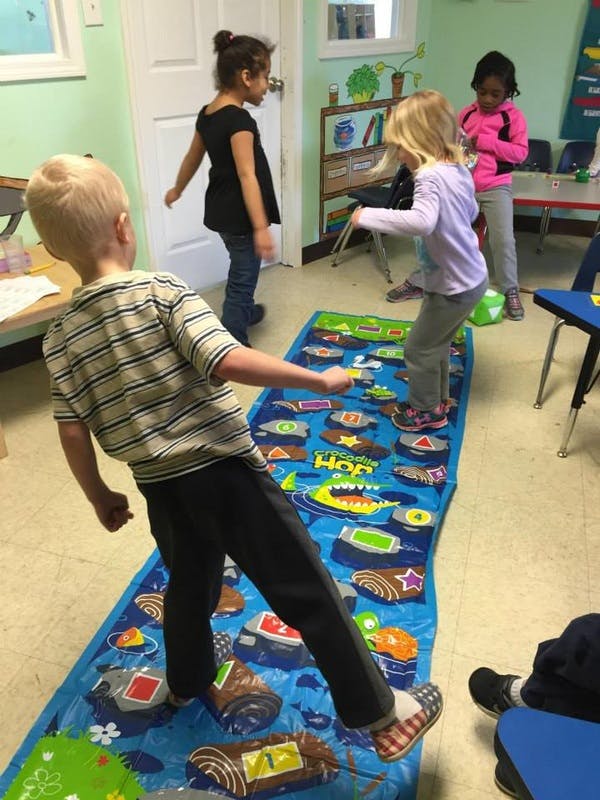 Children playing on a hopscotch mat in a classroom