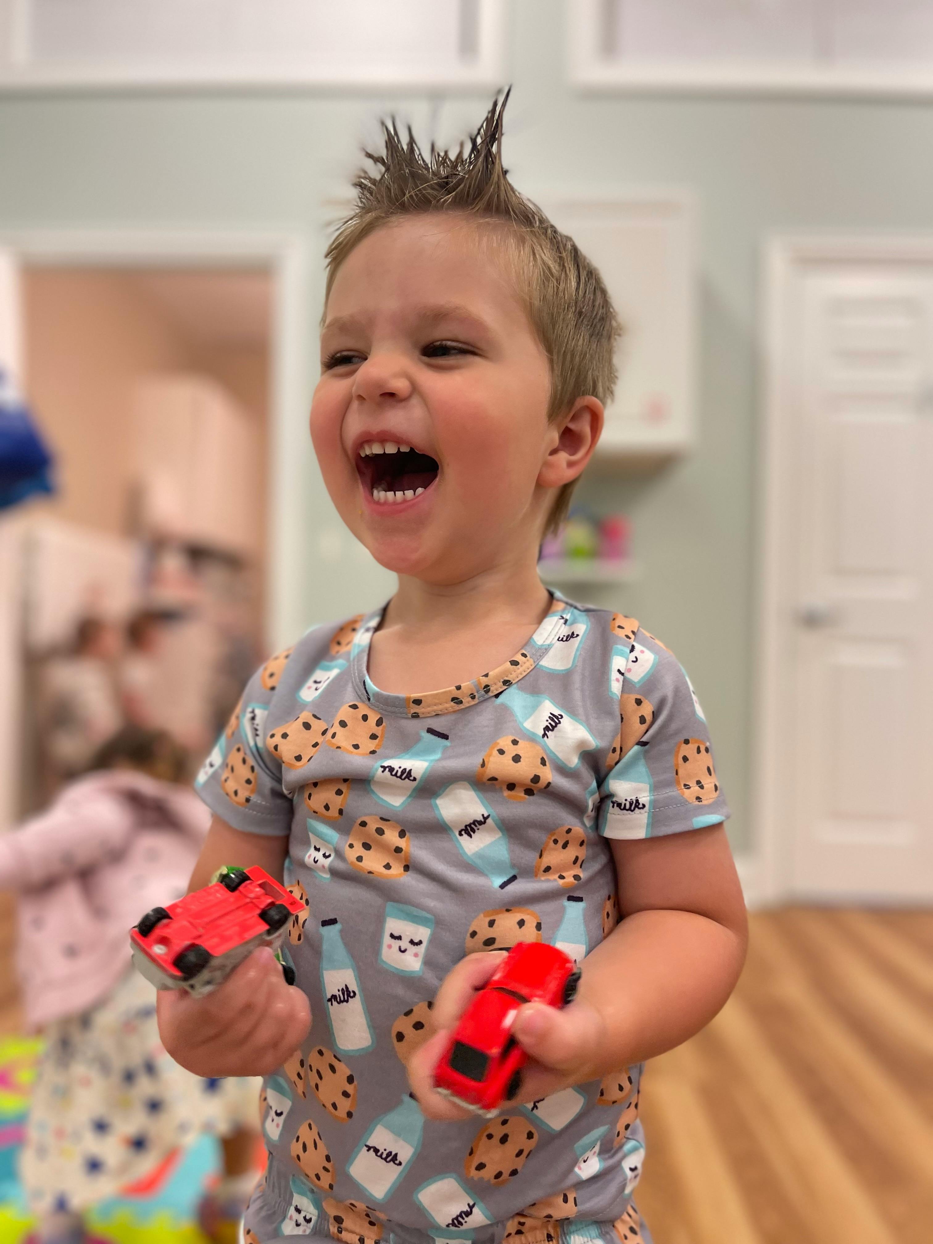 Child with spiky hair holding two toy cars