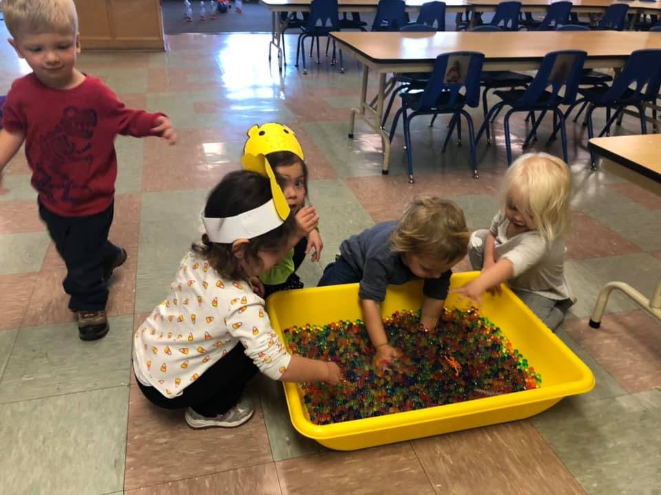 Children playing with colorful beads in a yellow bin