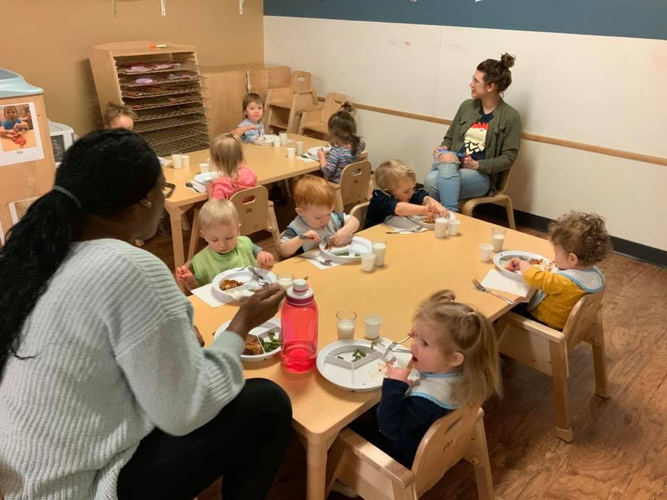 Adults and children eating at tables in a classroom