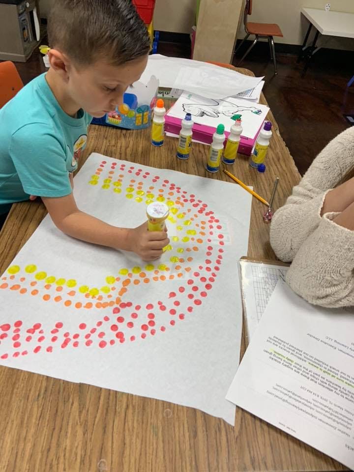 Child making dots on paper with a yellow marker