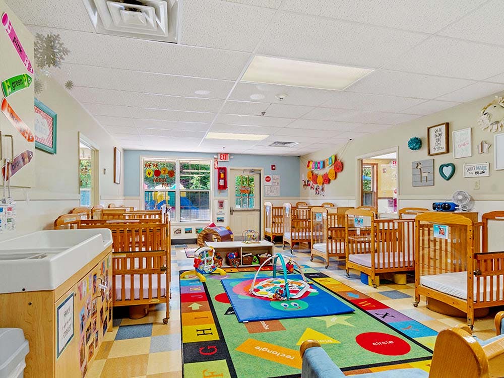 daycare classroom with multiple cribs, a changing station, and a colorful rug