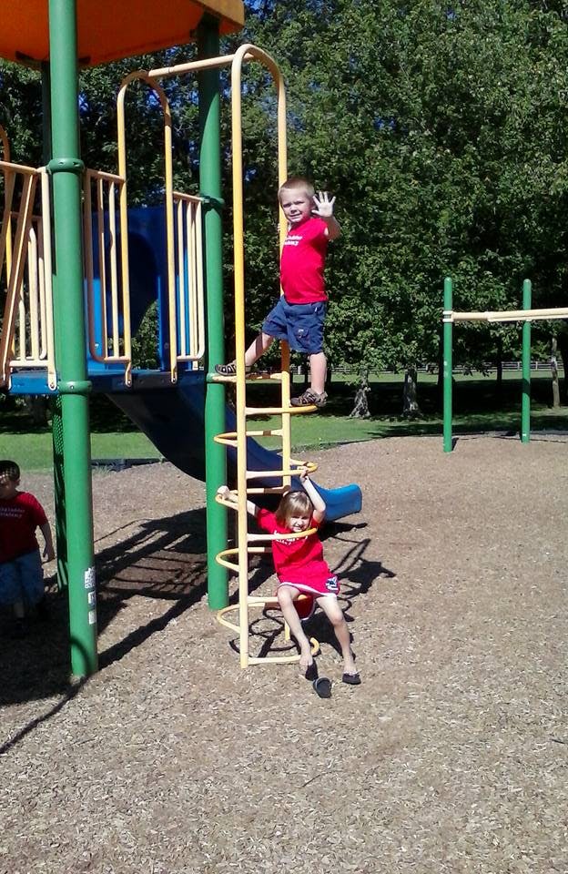 Two children on playground equipment, one climbing up, one climbing down