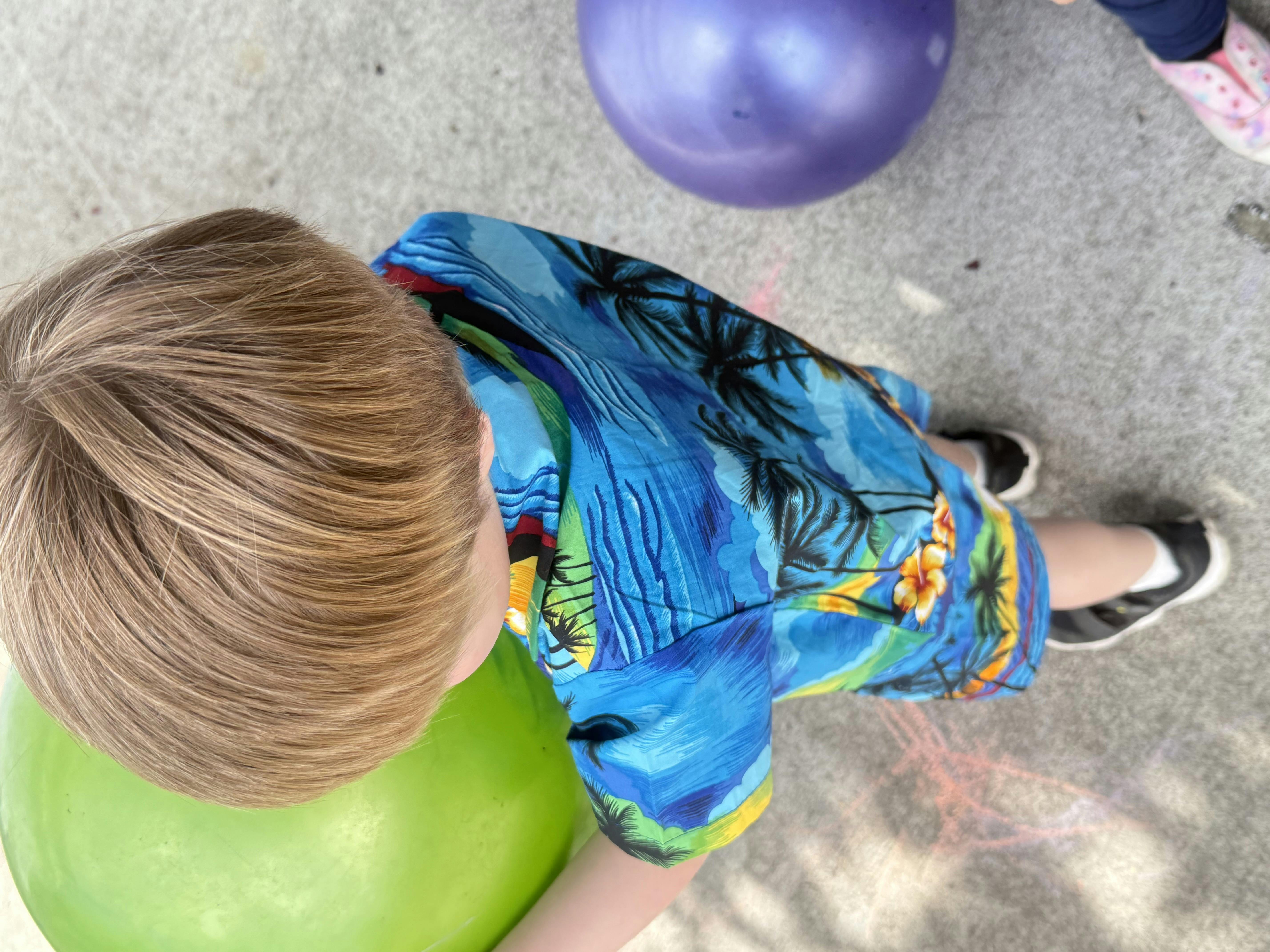 Child in a blue shirt leaning over a green ball