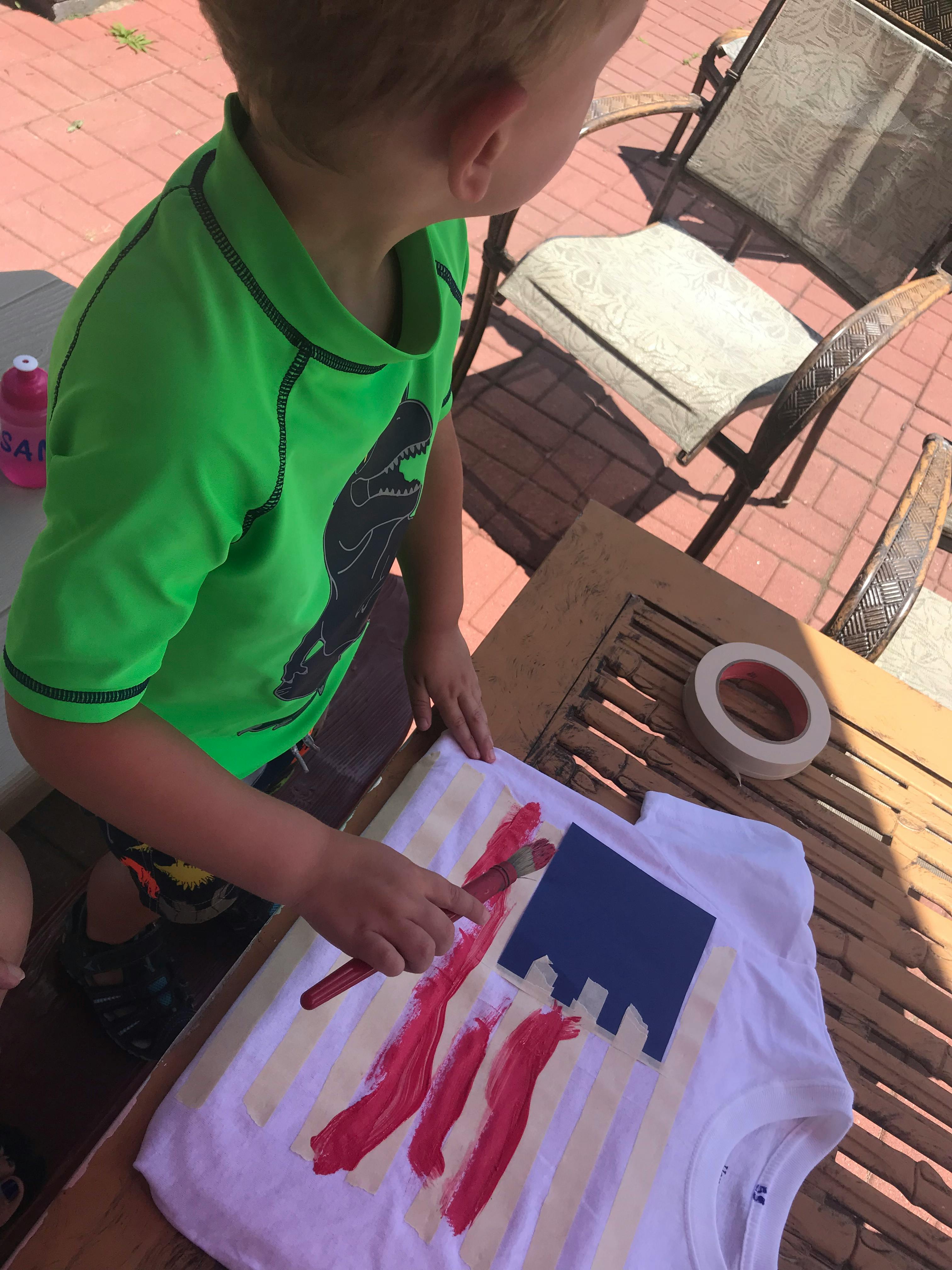 Child painting red stripes on a white t-shirt with a blue stencil