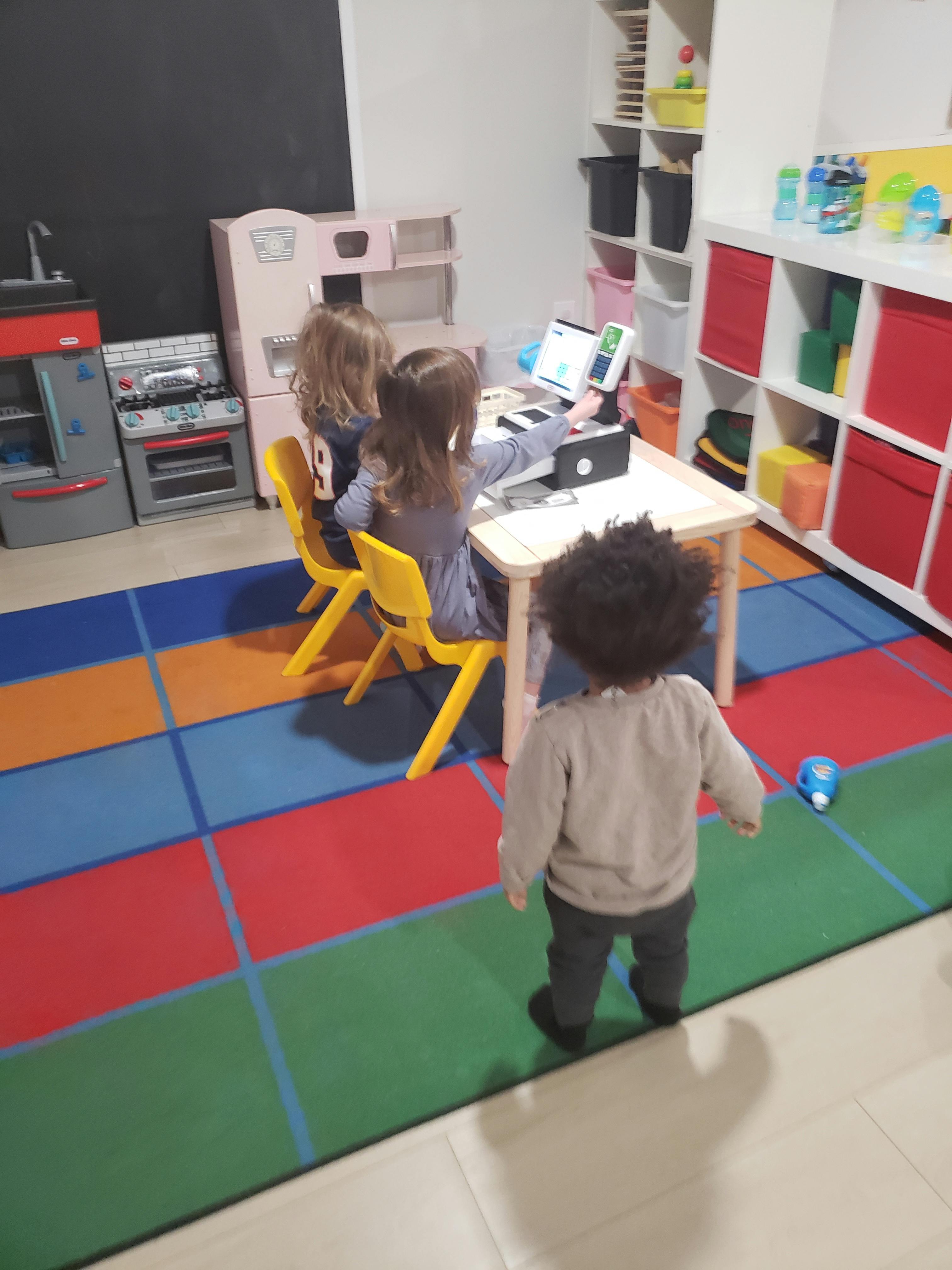 Two children at a table with a laptop, another child standing nearby