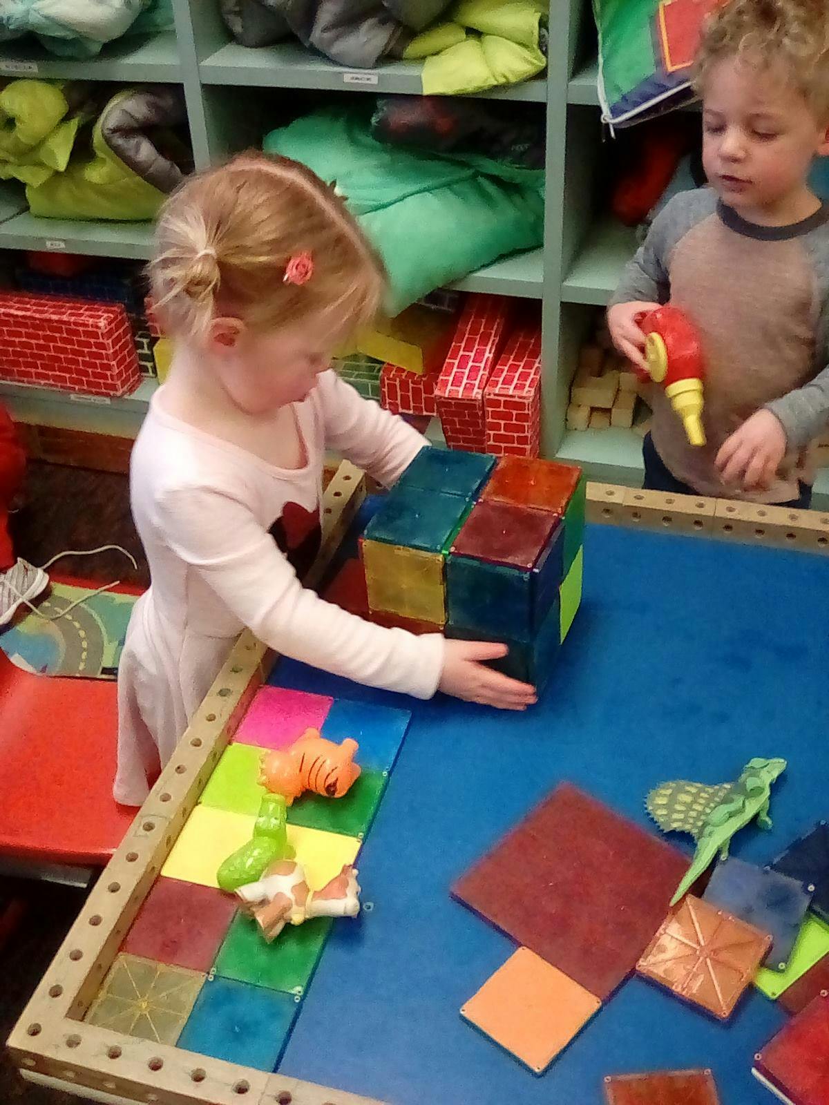 Child playing with colorful magnetic blocks, another child in background