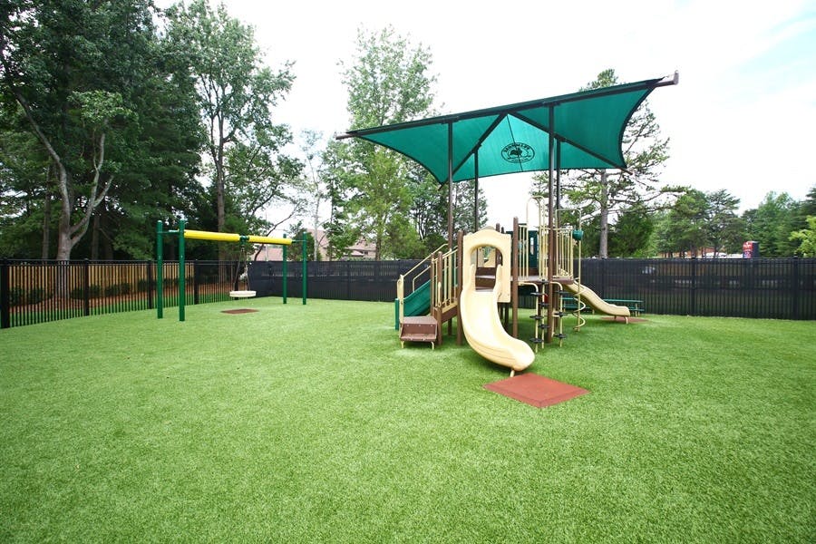 Playground with slides, swings, and a green shade canopy over artificial turf