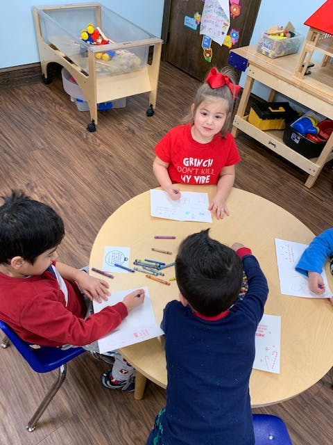 Three children drawing at a round table in a classroom