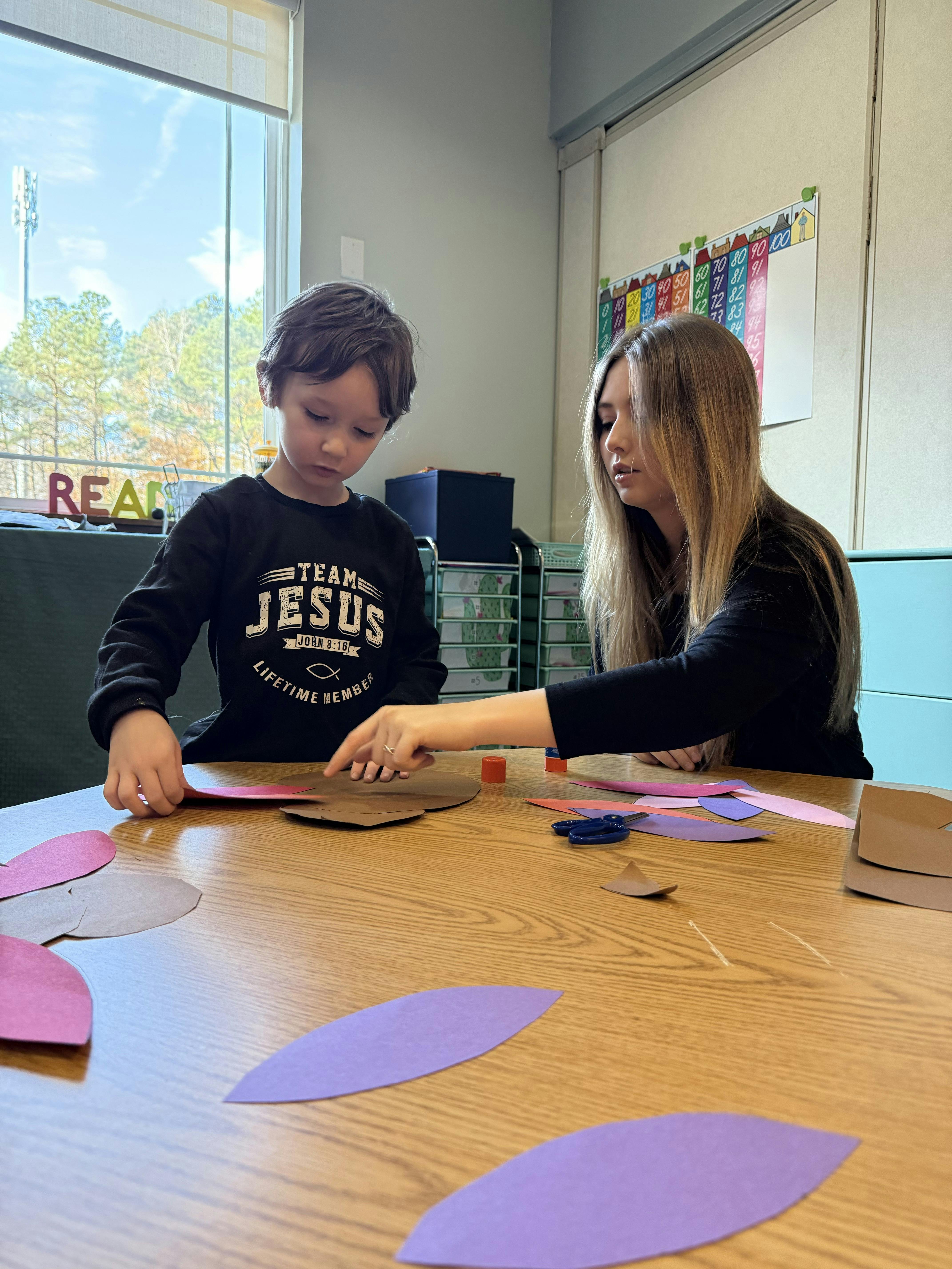 Child and person at a table working on a craft project with colored paper