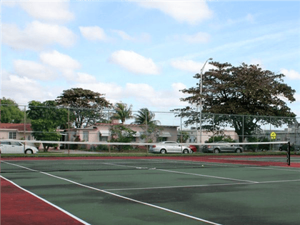 Tennis court with a net and cars parked in the background