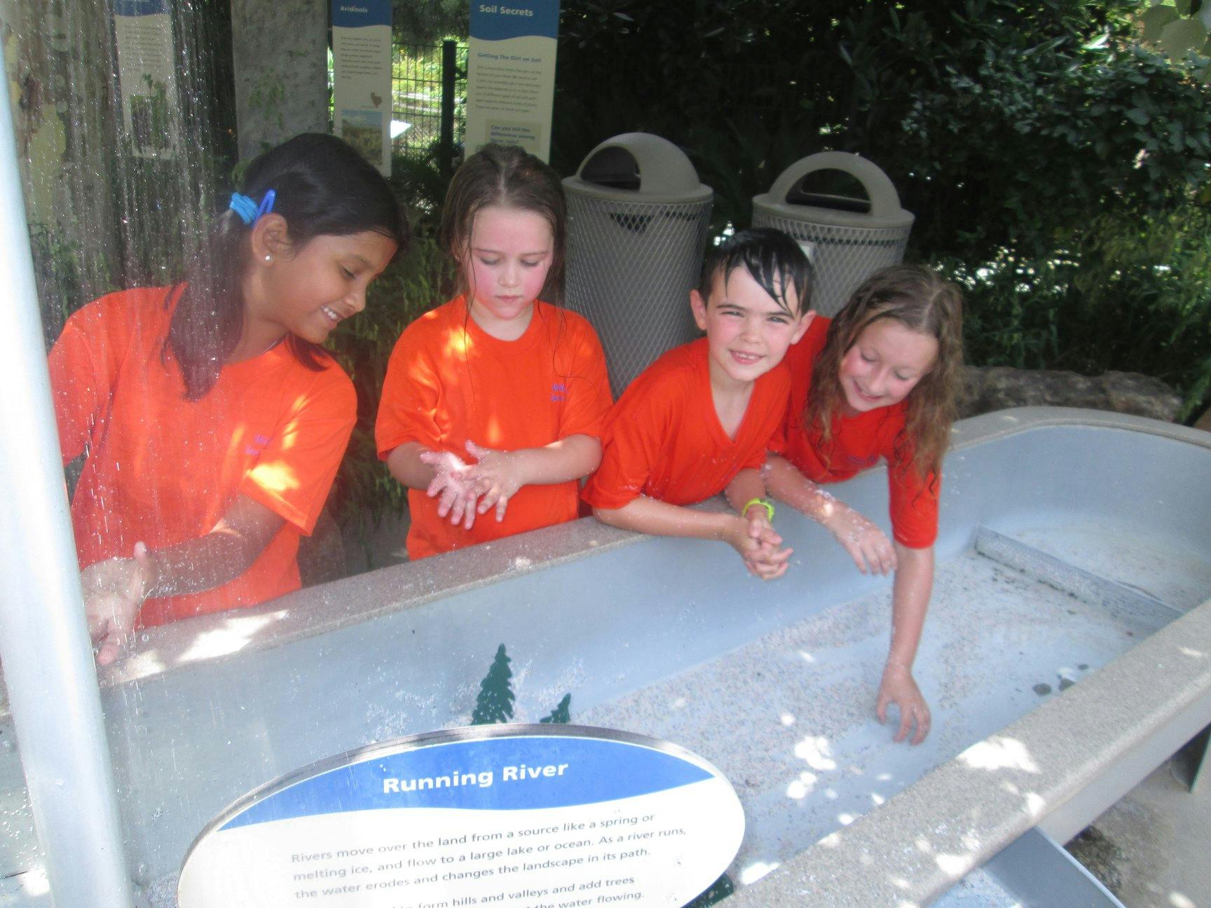 Four children playing in a water table with a sign that says "Running River"