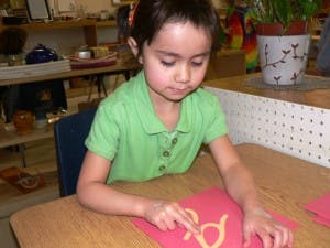 Child tracing a letter on red paper at a table