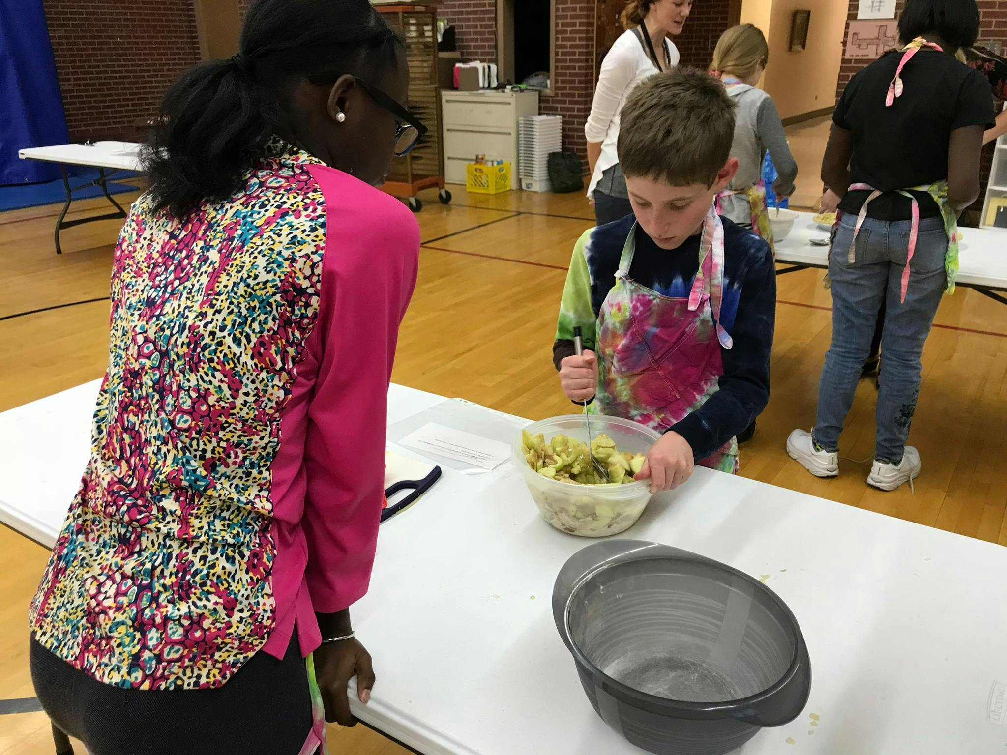 Person watching child mixing food in a bowl at a table