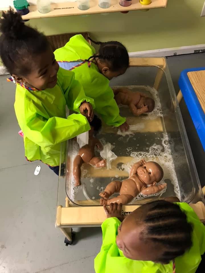 Children in green smocks playing with baby dolls in a water table