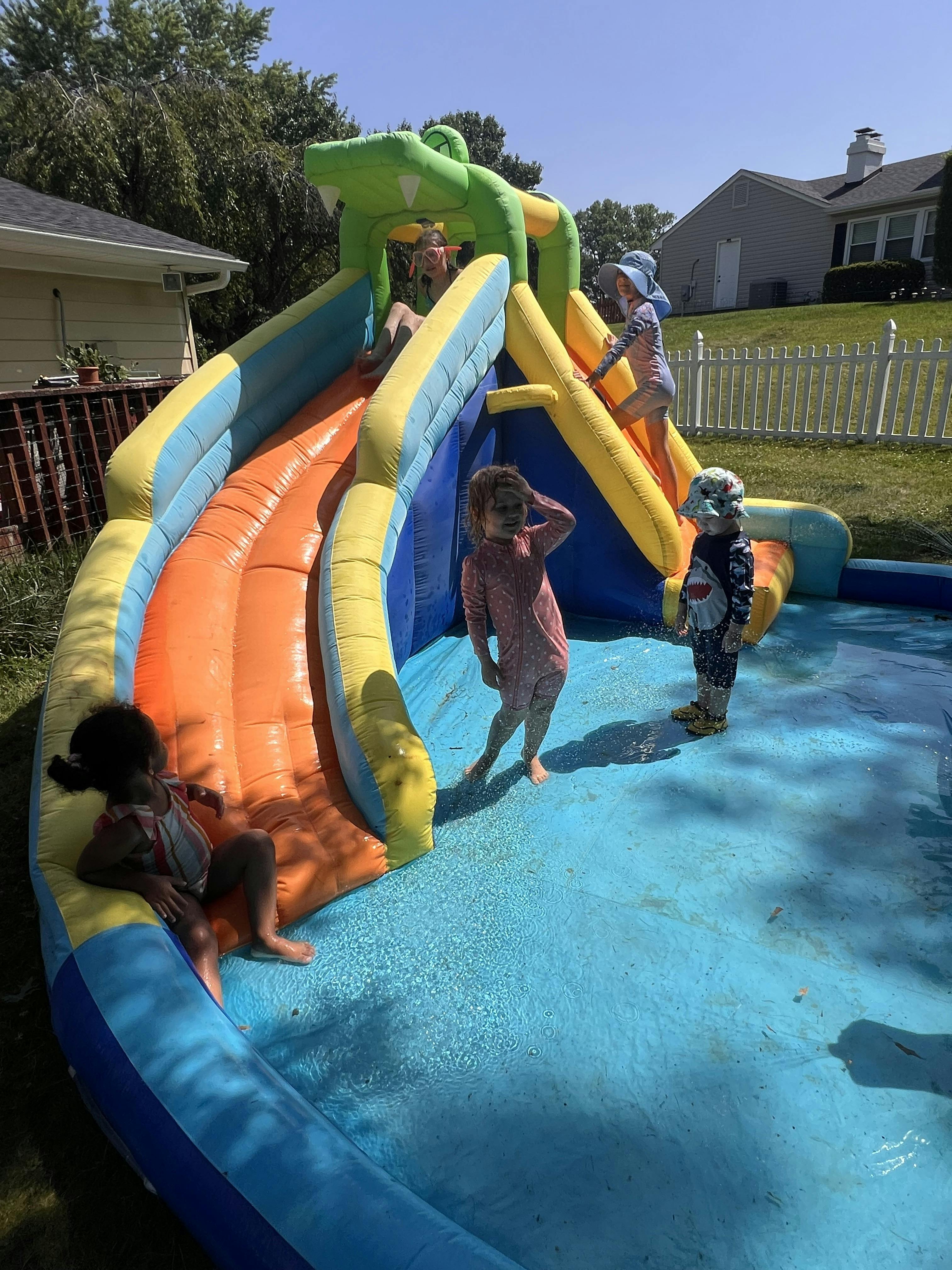 Children playing in an inflatable water slide in a backyard