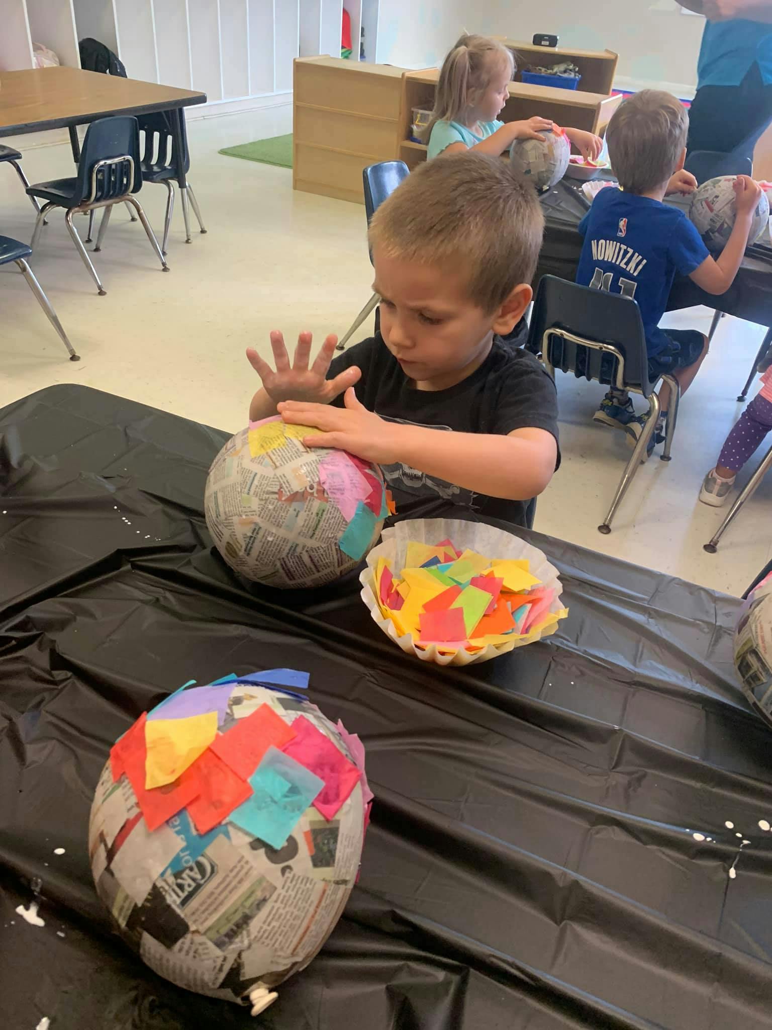 Child decorating a paper mache balloon with colorful paper squares