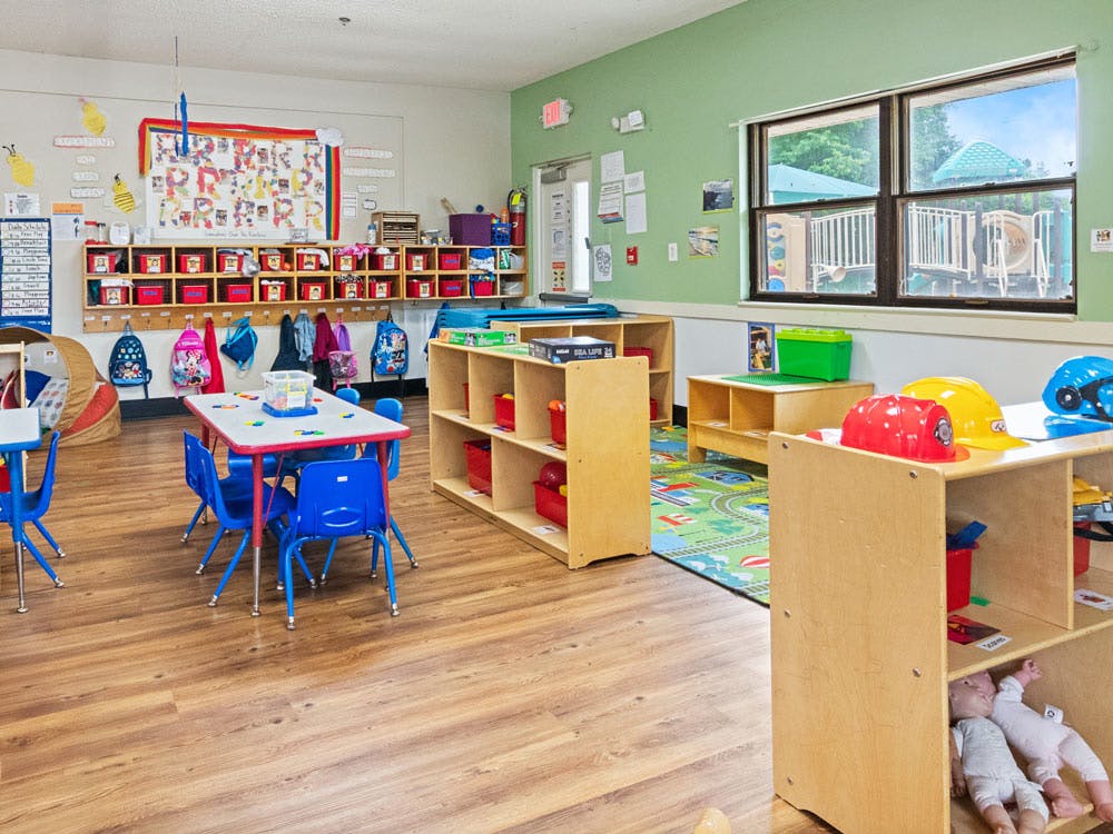 Classroom with tables, chairs, cubbies, shelves, and a window overlooking a playground