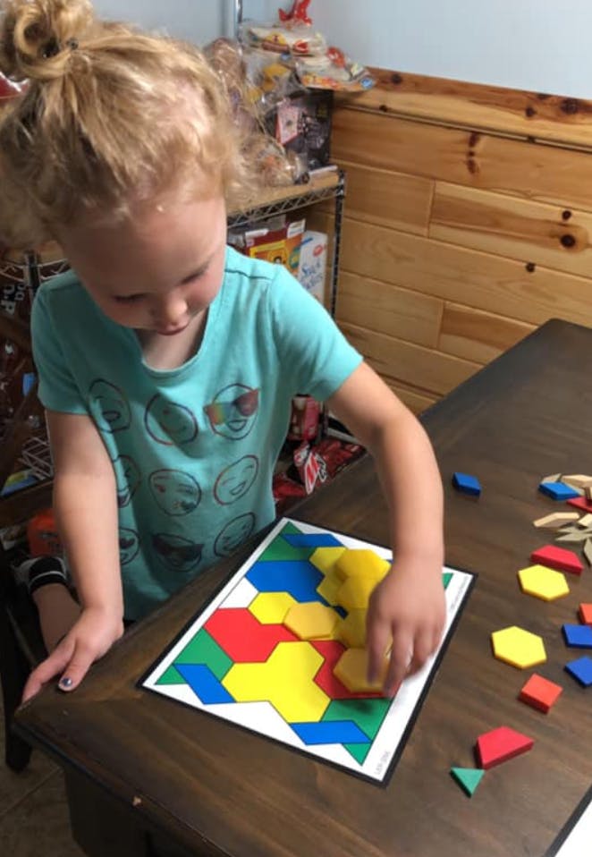 Child playing with colorful geometric shape puzzle pieces on a wooden table