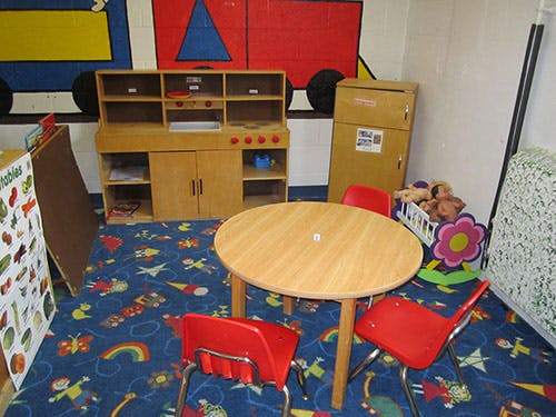 Playroom with a small wooden table and red chairs, toy kitchen, and patterned carpet